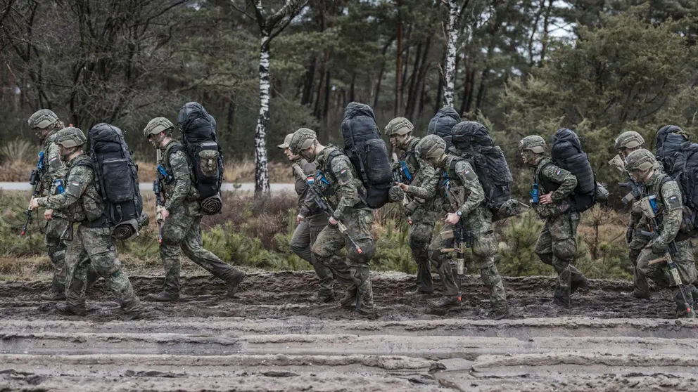 Militairen lopen over een modderig pad.