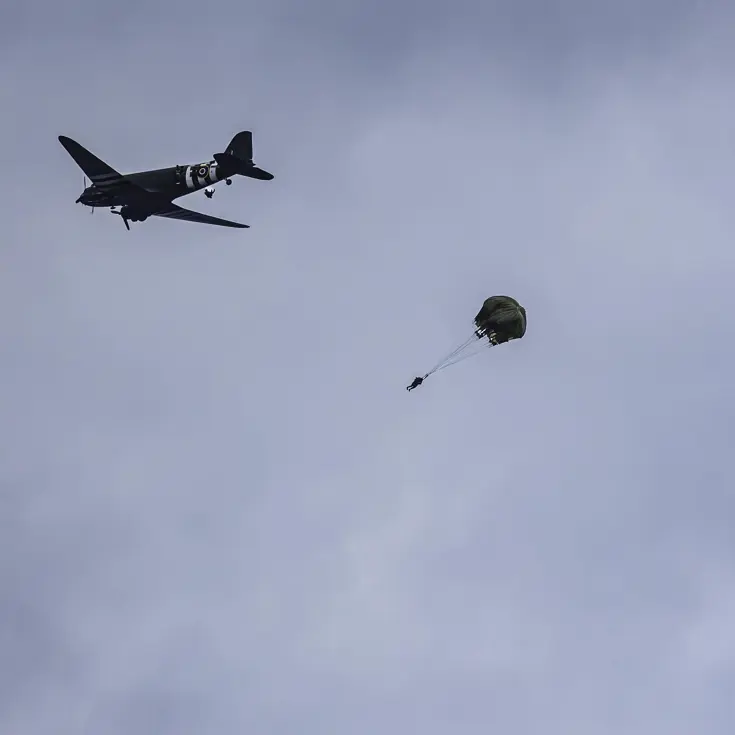  parachutisten springen uit een oud tweemotorig vliegtuig.