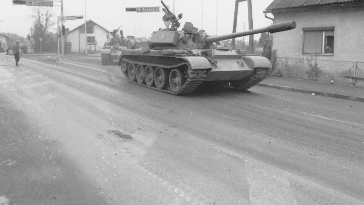 een tank rijdt langs een huis, met op de achtergrond een verkeersbord met daarop Zagreb.