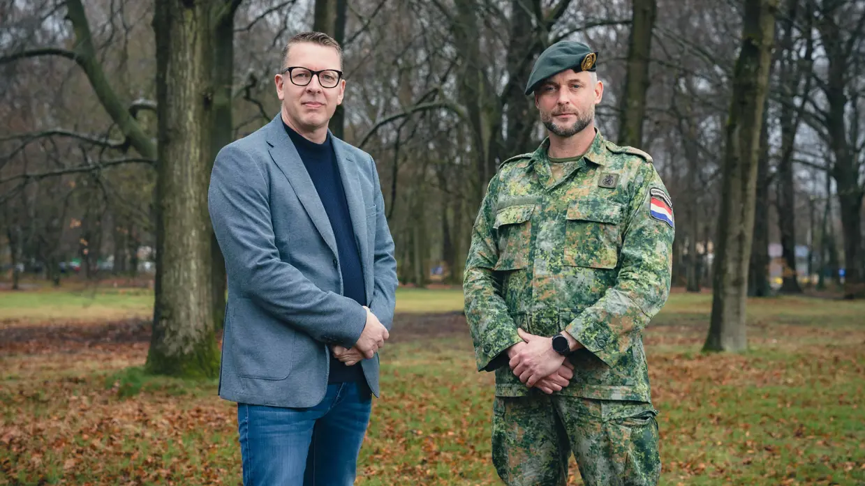 Portretfoto van projectleider Michel en majoor Jean. De twee staan naast elkaar en hebben hun handen voor zich. Daarachter een bosrijke omgeving.