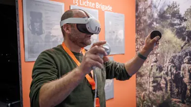 Kalende man in groene trui met een VR-bril op en voorwerpen in beide handen.