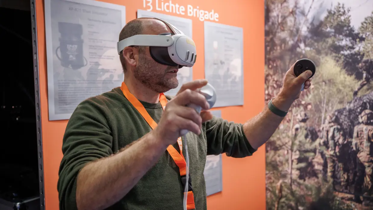 Kalende man in groene trui met een VR-bril op en voorwerpen in beide handen.