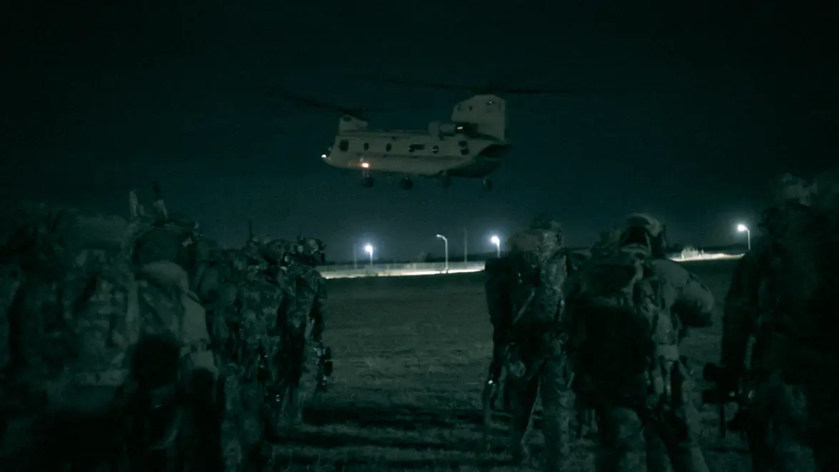 Alt-tekst: Chinook stijgt in duisternis op, op de voorgrond landmachtmilitairen. 
