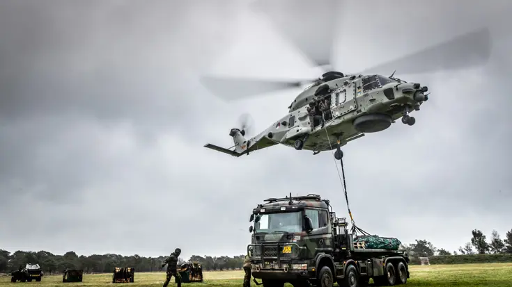 Gevechtshelikopter met draaiende rotorbladen tilt vracht van vrachtwagen.