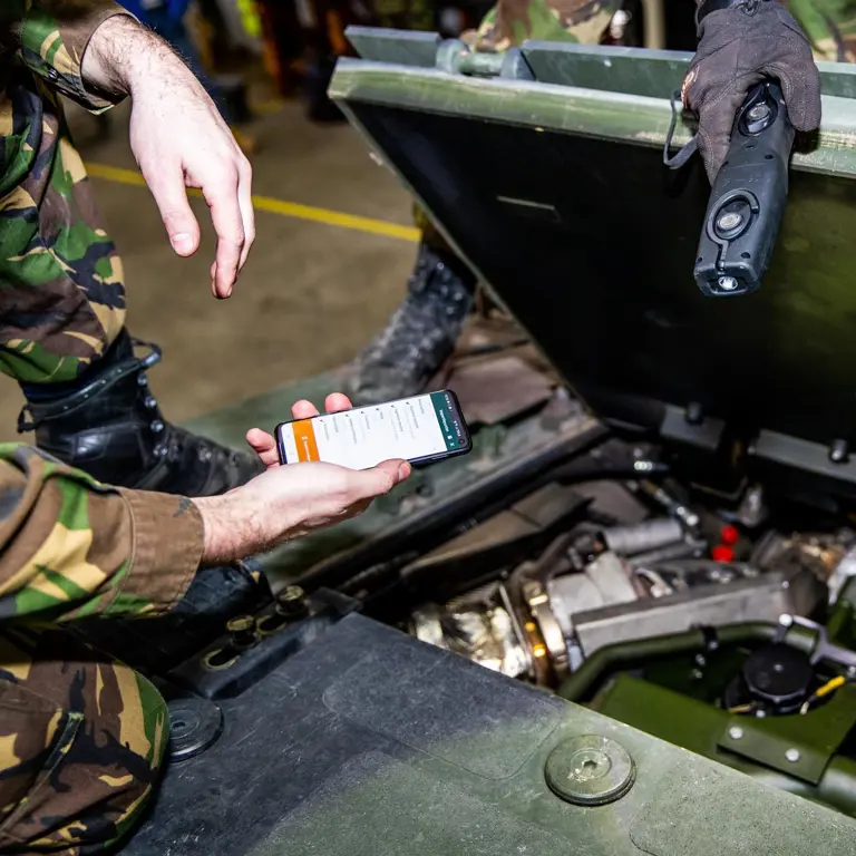 Monteur met telefoon in hand tijdens onderhoud voertuig.