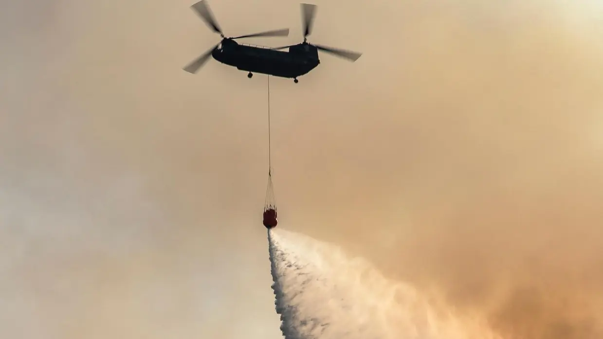 Chinook tegen oranje lucht stort water via waterzak onder het toestel.