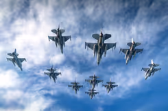 Een formatie F-16 vliegtuigen van onderaf gezien. Een blauwe lucht op de achtergrond met enkele wolken.