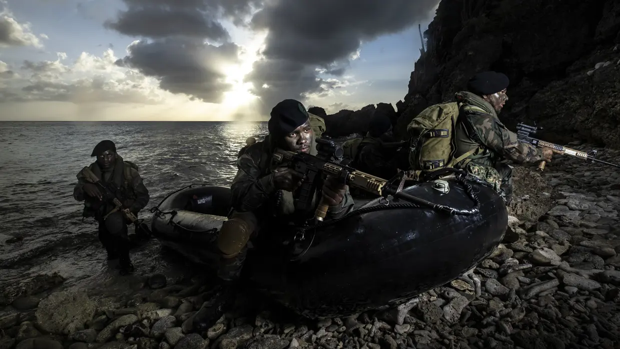 3 militairen met geweren komen in een rubber boot aan land.