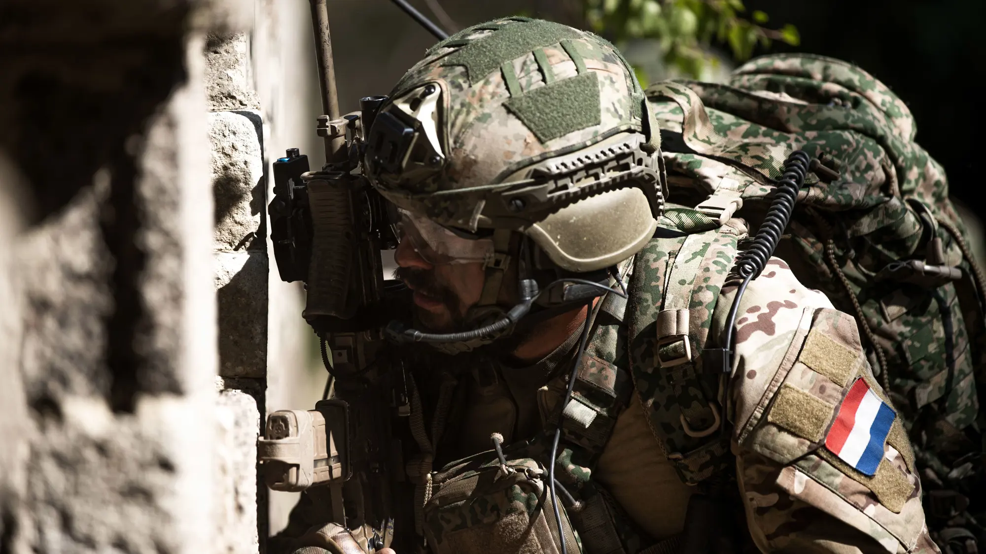 Militair kijkt om hoek van gebouw.