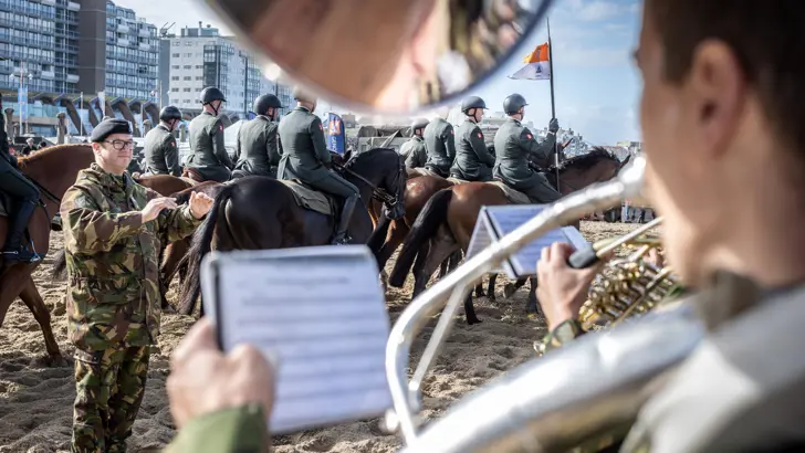 Militairen spelen muziek tijdens het oefenen met paarden op het strand.