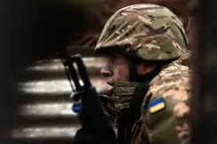 Oekraïense militair zit gehurkt met wapen voor zich.