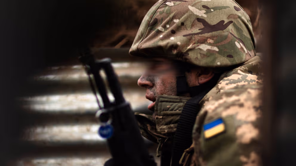 Oekraïense militair zit gehurkt met wapen voor zich.