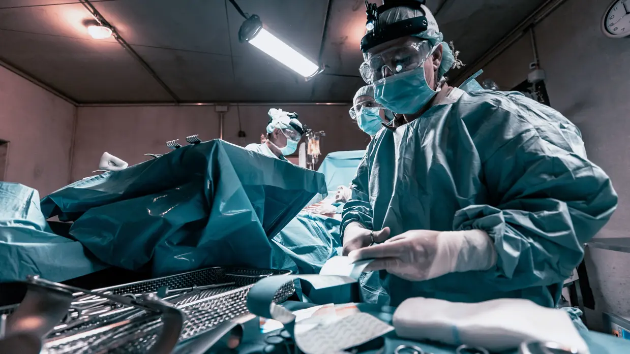 Een arts in groene operatiekleding knipt een verband.