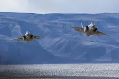 2 F-35 jachtvliegtuigen vliegen boven water tegen een achtergrond van bergen in blauw licht.