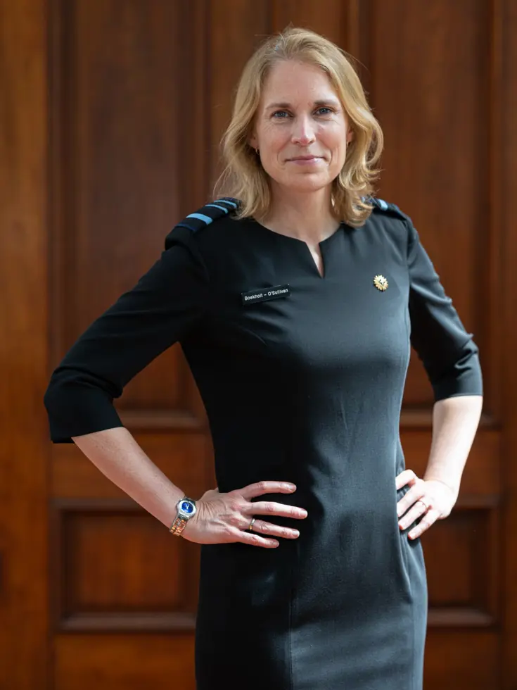 Boekholt-O’Sullivan staat met haar handen in haar zij. Ze draagt een zwarte jurk met rangonderscheidingstekens. 