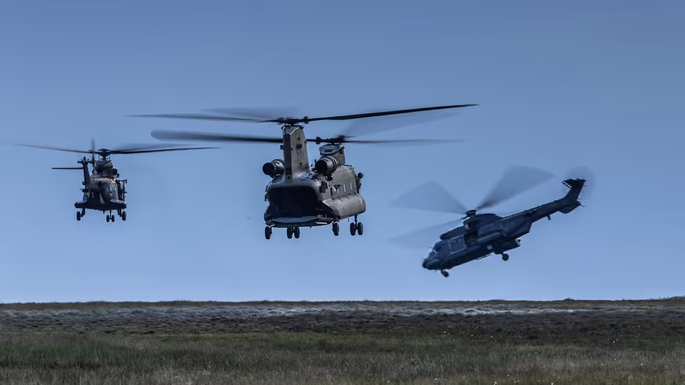 Drie helikopters vliegen laag boven de grond.