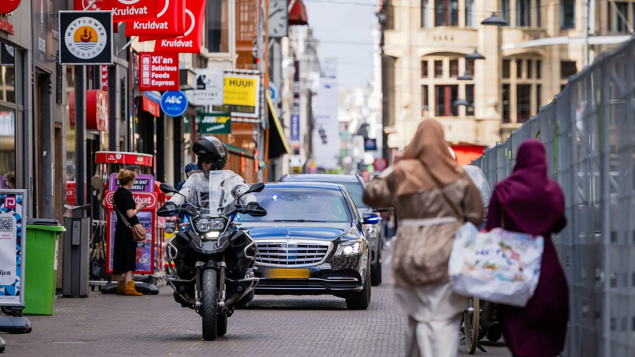 Twee auto’s met geblindeerde ramen rijden achter elkaar door een winkelstraat in Den Haag.