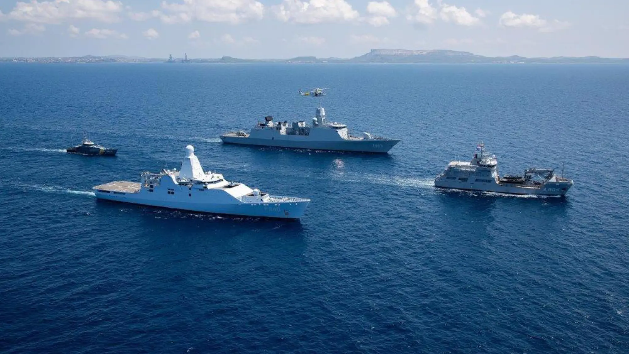4 marineschepen varen in een ruitvorm op het water.