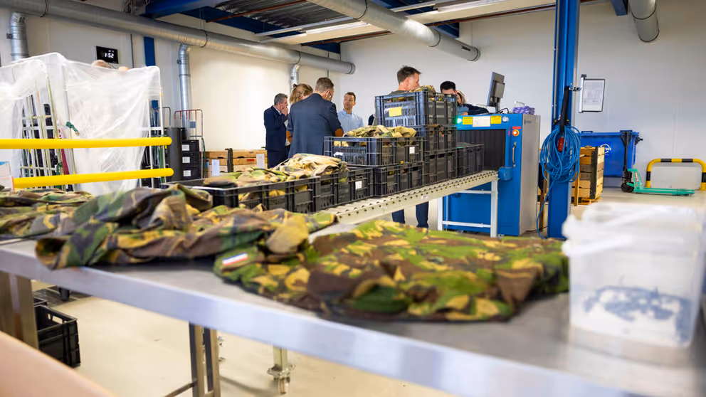 Oude Defensie-uniformen liggen in loods op tafels en in kratten uitgestald.