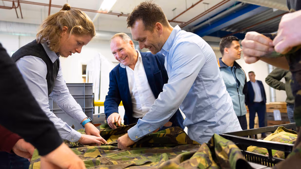 Medewerkers van het DJI raken de militaire uniformen aan, die op een glimmende tafel liggen.