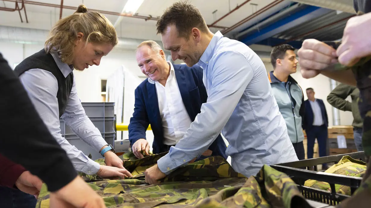 Medewerkers van het DJI raken de militaire uniformen aan, die op een glimmende tafel liggen.