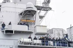 Militairen staan zwaaiend naast elkaar langs de reling van een marineschip.