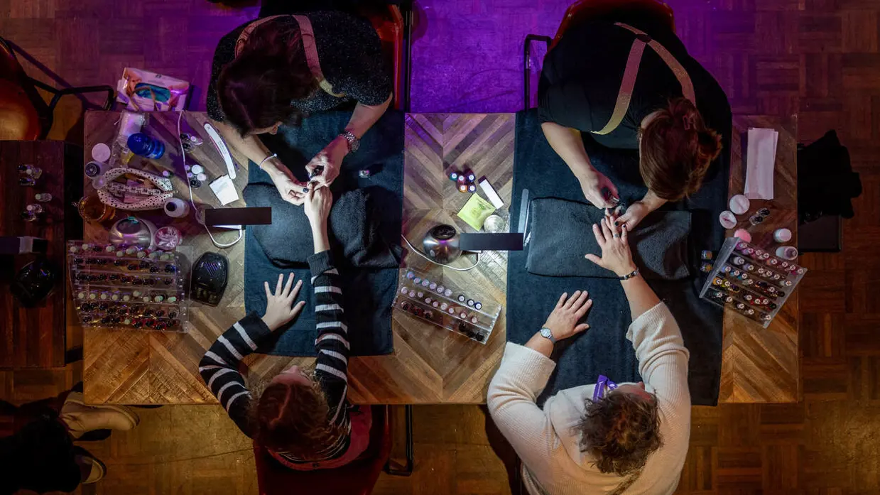 Twee dames krijgen een manicure, van bovenaf gezien en belicht door een klein lampje.