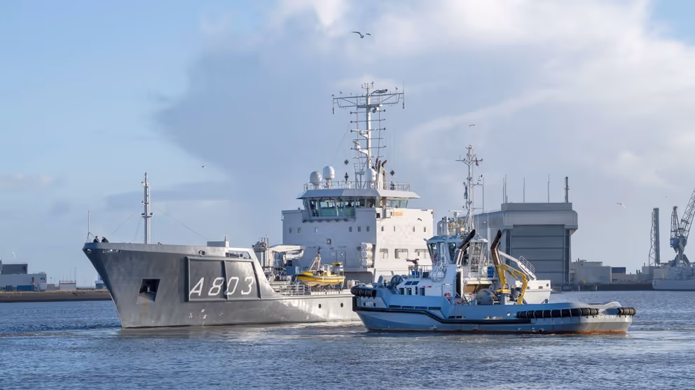 Een varende Zr.Ms. Luymes met een sleepboot erbij.