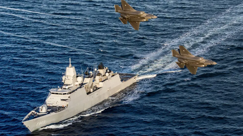 Zr.Ms. Tromp vaart op zee terwijl 2 gevechtsvliegtuigen er overheen vliegen.