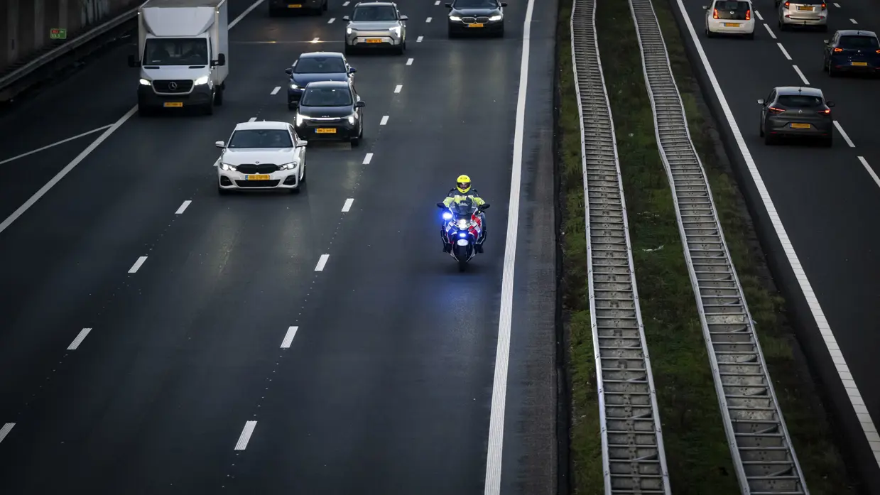 Een motorbegeleider van de Koninklijke Marechaussee rijdt met zwaailicht over de snelweg terwijl het overige verkeer ruimte maakt.