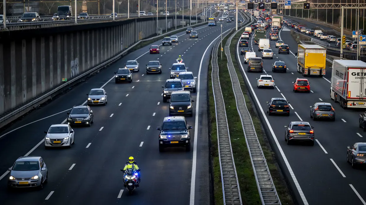 Een motorbegeleider van de Koninklijke Marechaussee rijdt voor een colonne dienstvoertuigen over de snelweg.