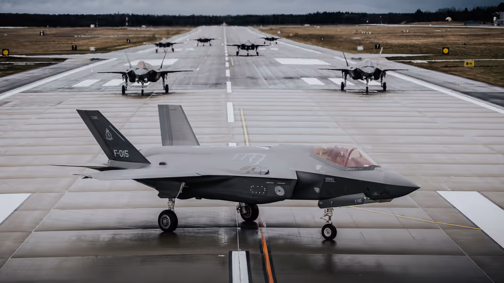 7 F-35's staan op een landingsbaan. De voorste is zichtbaar vanaf de zijkant. Van de overige 6 is de neus te zien.