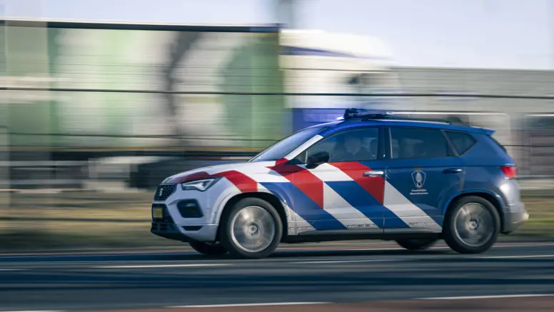 Een dienstvoertuig met zwaailicht dat snel langs een vangrail rijdt.