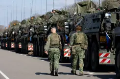 Rij militaire voertuigen. Daarnaast lopen 2 militairen.