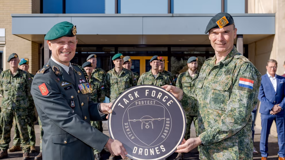 Luitenant-generaal Jan Swillens houdt met collega rond bord vast met de tekst: Task Force Drones. Opgestelde militairen op de achtergrond.