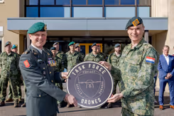 Luitenant-generaal Jan Swillens houdt met collega rond bord vast met de tekst: Task Force Drones. Opgestelde militairen op de achtergrond.
