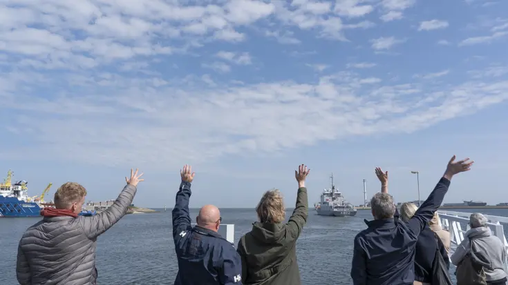 Mensen zwaaien vanaf de kade een marineschip uit.