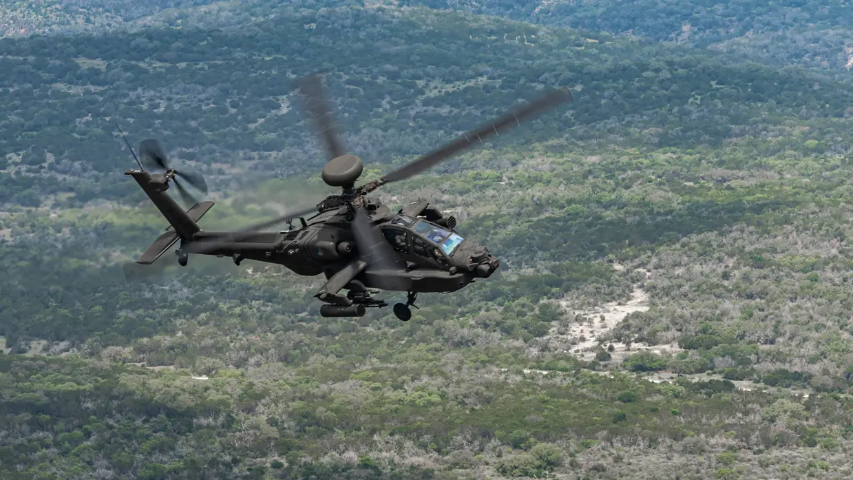 Een Apache vliegend boven begroeide heuvels.