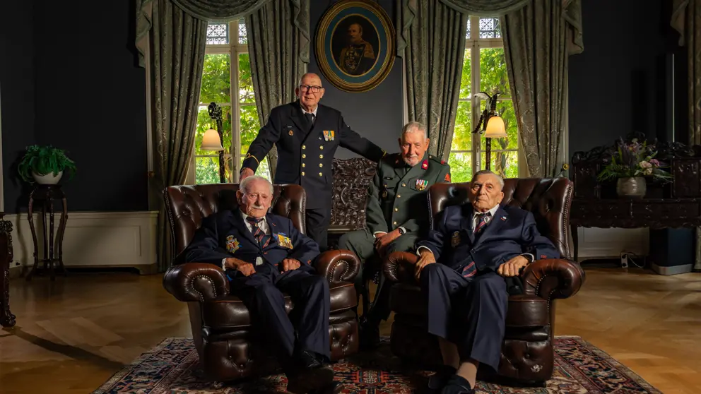 4 veteranen poseren, 2 van hen zitten in een stoel.