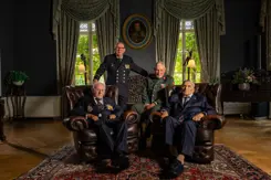 4 veteranen poseren, 2 van hen zitten in een stoel.