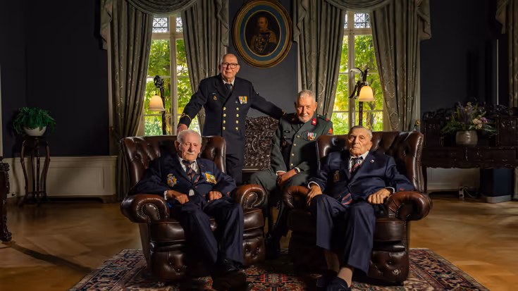 4 veteranen poseren, 2 van hen zitten in een stoel.