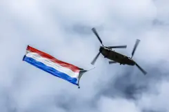 Vliegende Chinook-transporthelikopter van onderop gezien met Nederlandse vlag aan onderkant bevestigd.