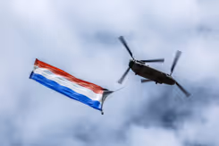 Vliegende Chinook-transporthelikopter van onderop gezien met Nederlandse vlag aan onderkant bevestigd.