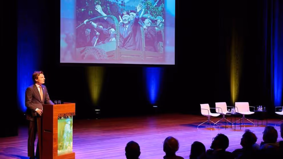 Minister Brekelmans spreekt vanaf podium volle zaal toe.