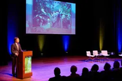 Minister Brekelmans spreekt vanaf podium volle zaal toe.