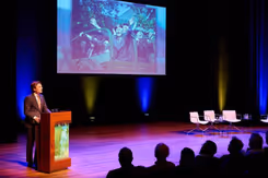 Minister Brekelmans spreekt vanaf podium volle zaal toe.