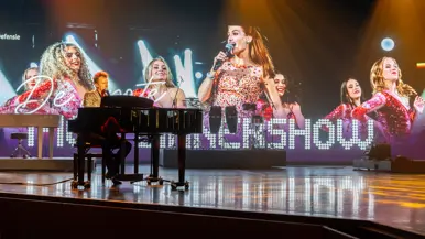 Alt: Links een zanger achter een piano. Rechts een soort toren met daarop smakelijke hapjes. 