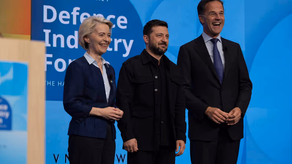 Een vrouw en twee mannen staan lachend naast elkaar op een podium.