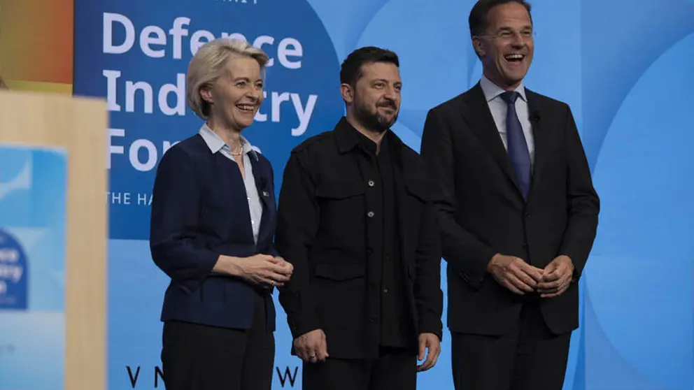 Een vrouw en twee mannen staan lachend naast elkaar op een podium.
