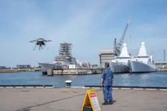 Militair staat op kade en kijkt naar drone die opstijgt.